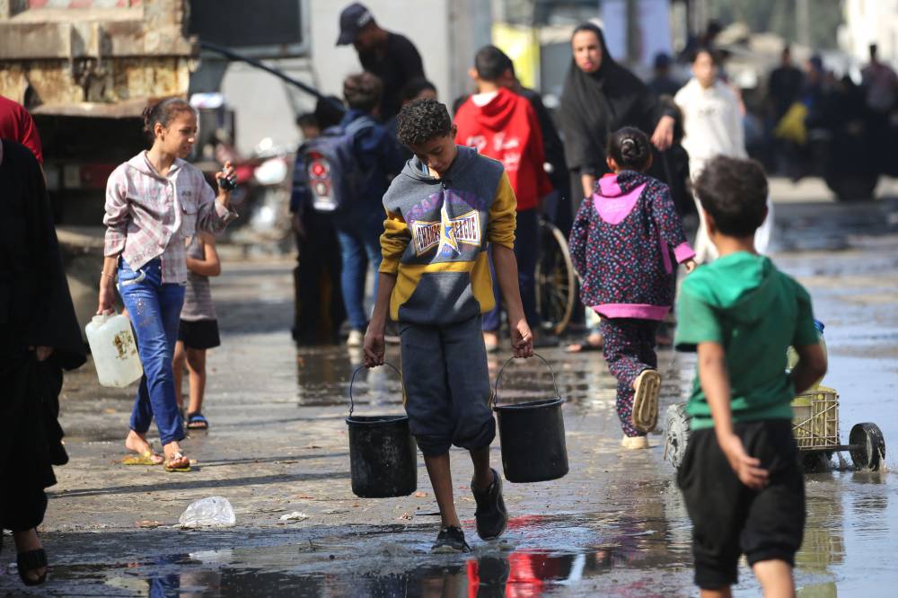شاب يحمل دلوين من الماء في مخيم للنازحين النصيرات 