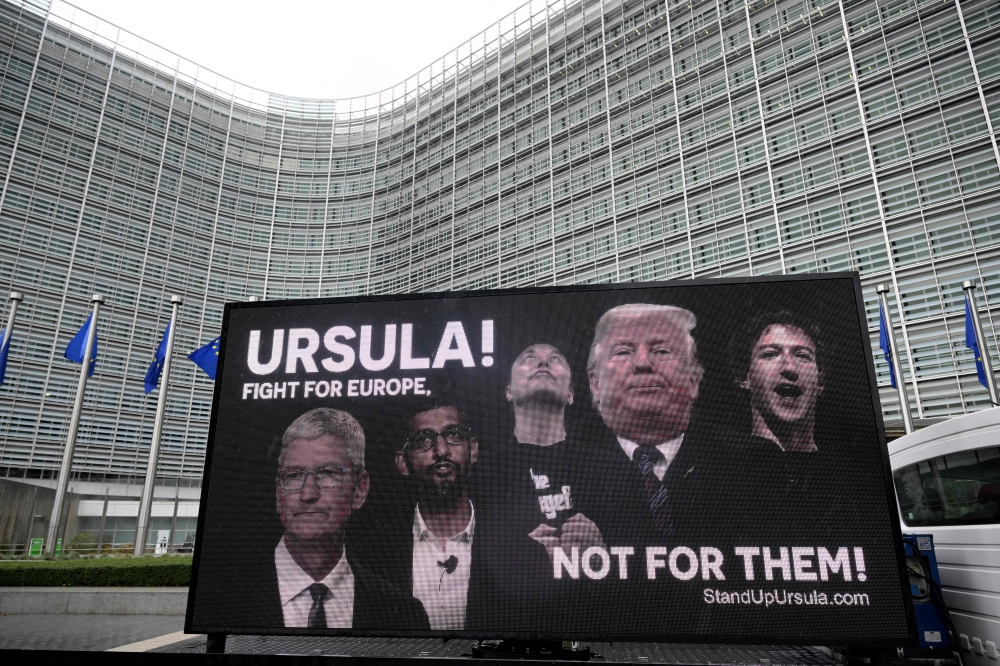 نشطاء يعرضون لوحة إعلانية متنقلة تحث رئيس المفوضية على الوقوف في وجه عمالقة التكنولوجيا الأمريكيين (أ.ف.ب)