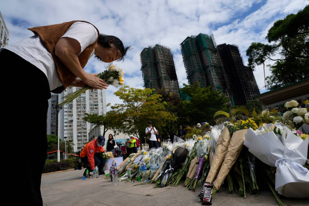 A woman bows as she offers flowers near the site of a deadly fire at Wang Fuk Court, a residential estate in the Tai Po district of Hong Kong's New Territories on Tuesday, Dec. 2, 2025. (AP Photo/Ng Han Guan)