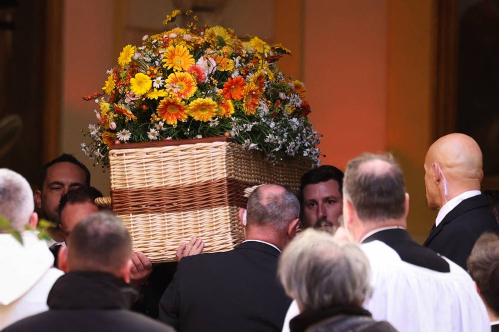 مشيعون يحملون النعش بعد انتهاء مراسم الجنازة بكنيسة نوتردام دي لاسومبشن (أ.ف.ب)  