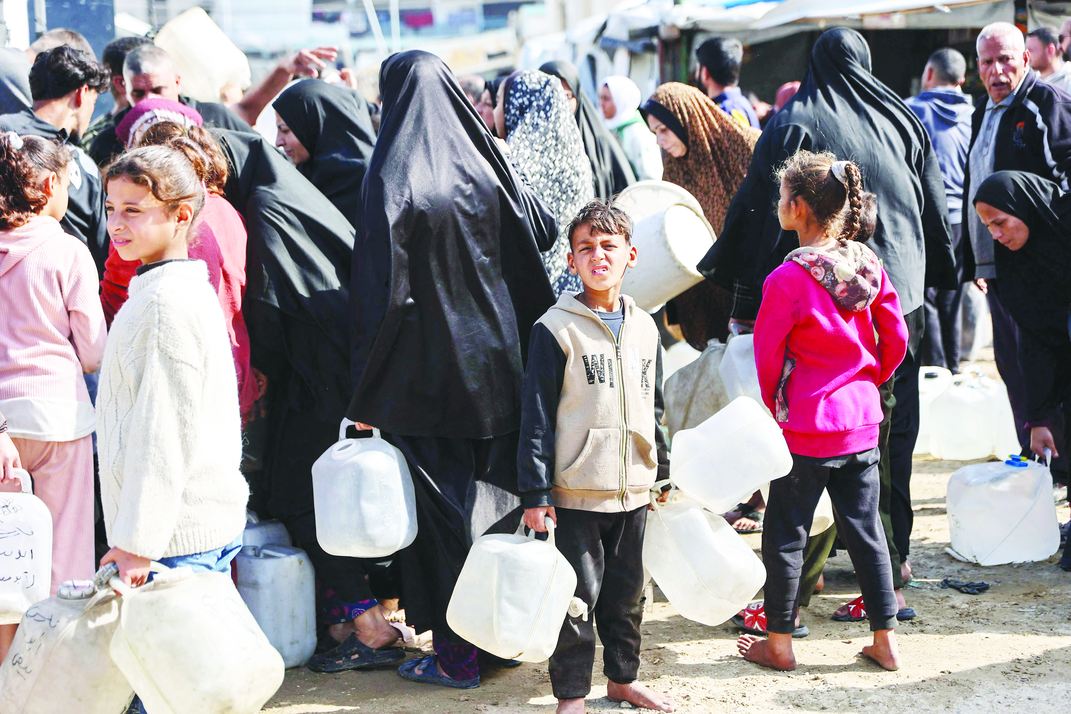 فلسطينيون نازحون ينتظرون تعبئة جالونات المياه في مخيم الرمال بمدينة غزة 