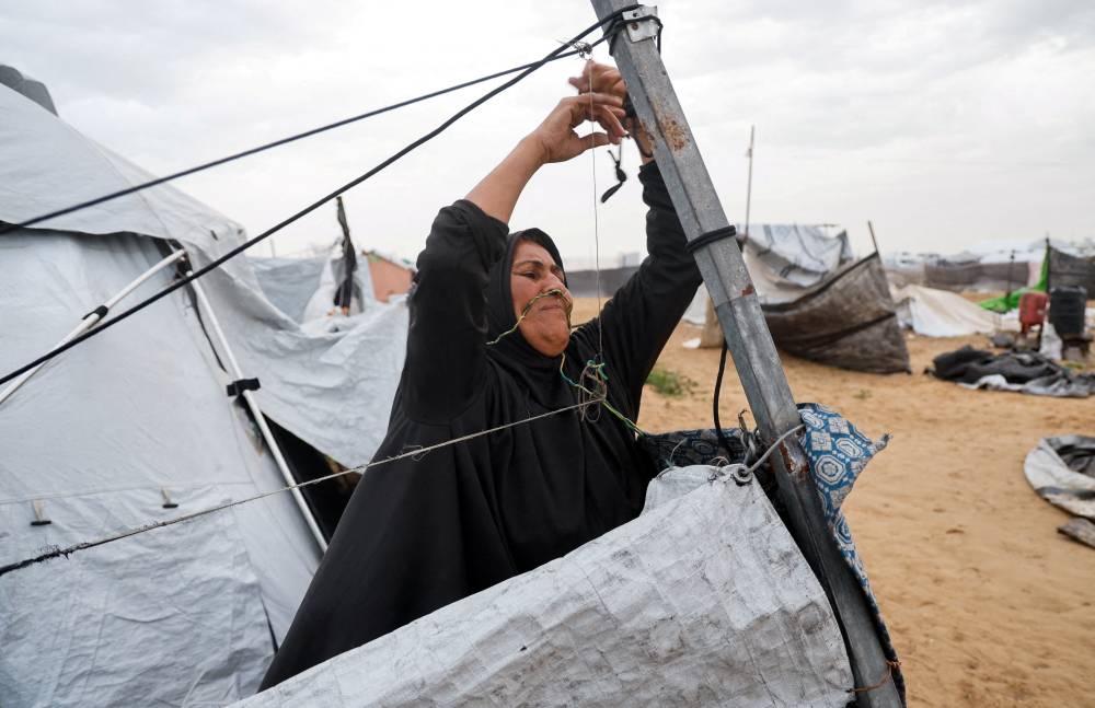 (رويترز)  امرأة تثبت خيمتها في مخيم  للنازحين خلال يوم عاصف بخان يونس